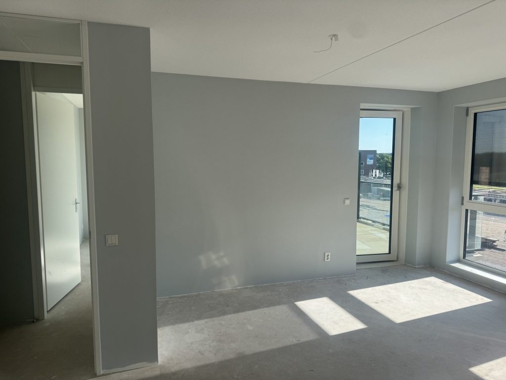Lichtgrijs gesausde wanden in een nieuw appartement met een balkondeur en een betonvloer