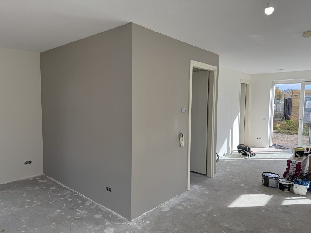 Nieuwbouwwoning met een grijs gesausde wand rond de meterkast en verfemmers op de vloer