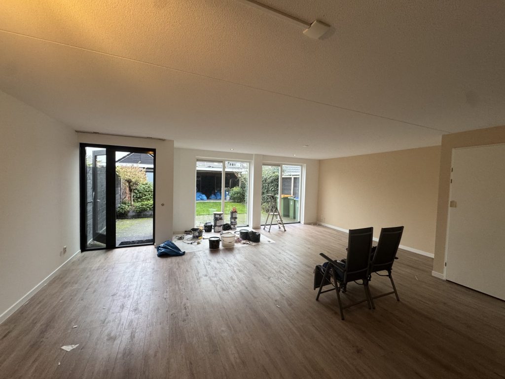 Ruime woonkamer met lichte wanden, laminaat en tuindeuren, met verfemmers midden in de kamer