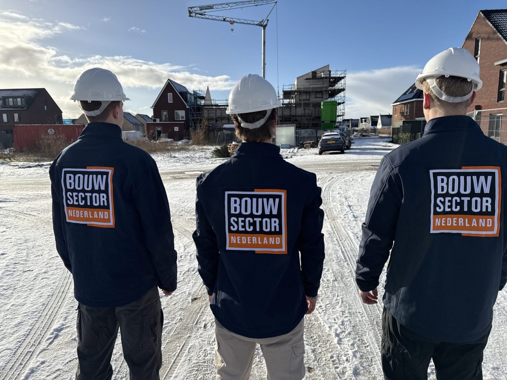 Drie vakmensen van Bouwsector Nederland met witte helm kijken naar woningen in aanbouw