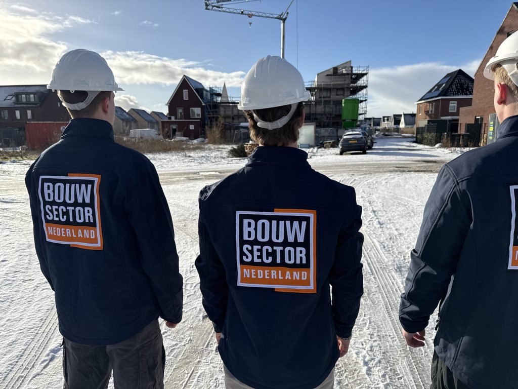Drie vakmensen van Bouwsector Nederland met witte helm in een straat met nieuwbouwhuizen in aanbouw